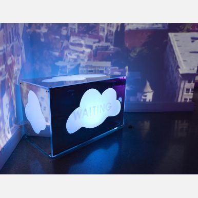 <em>Untitled (An Interstice)</em></br> Photograph of "Untitled (An Interstice)" by Michelle L Herman which depicts a rectangular box with a cloud-shaped cut out on each side that reveals a glowing, pulsating light underneath