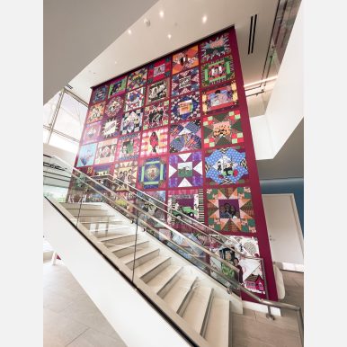 <em>Heritage Wall, Commissioned by the DC Public Library system</em> Photograph of the "Heritage Wall" commission installed at the Lamond-Riggs/Lillian J. Huff Community Library. The image is predominantly red and inspired by a quilt showing illustrations of area residents.